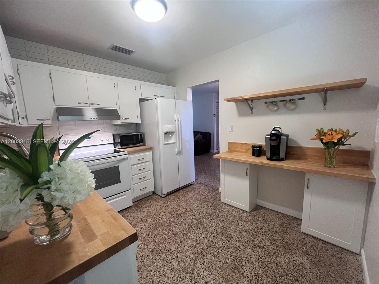 A kitchen features white cabinets, butcher block countertops, a white refrigerator, and carpeted flooring — 9840 SW 165th Ter, Miami FL 33157, MIAMI, FL