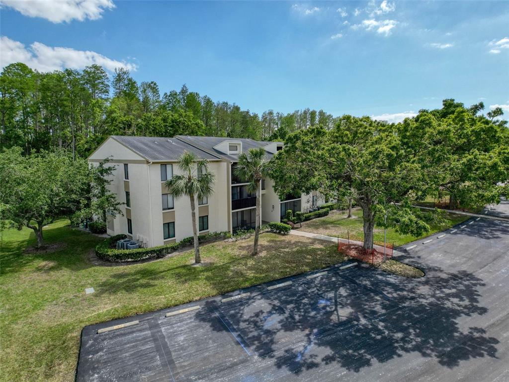 An exterior view of a multi-story apartment building with a parking lot and surrounding trees — 3188 LAKE PINE WAY S UNIT B1, TARPON SPRINGS, FL