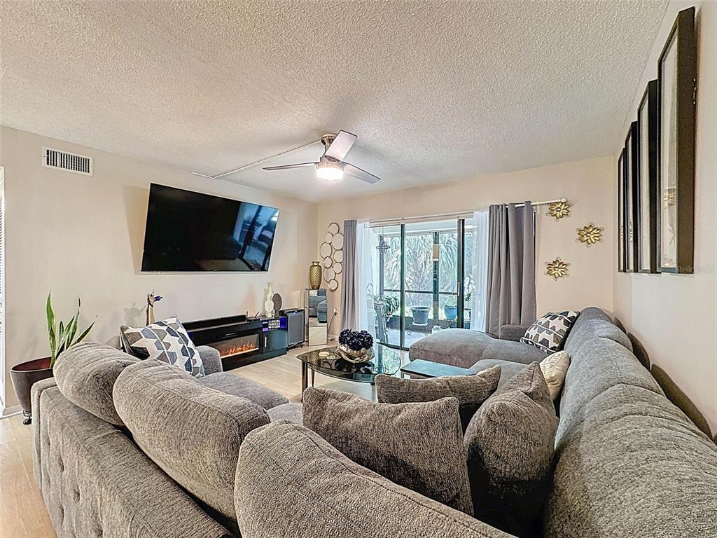 A living room features a large gray sectional sofa, a wall-mounted television, and sliding glass doors — 3188 LAKE PINE WAY S UNIT B1, TARPON SPRINGS, FL