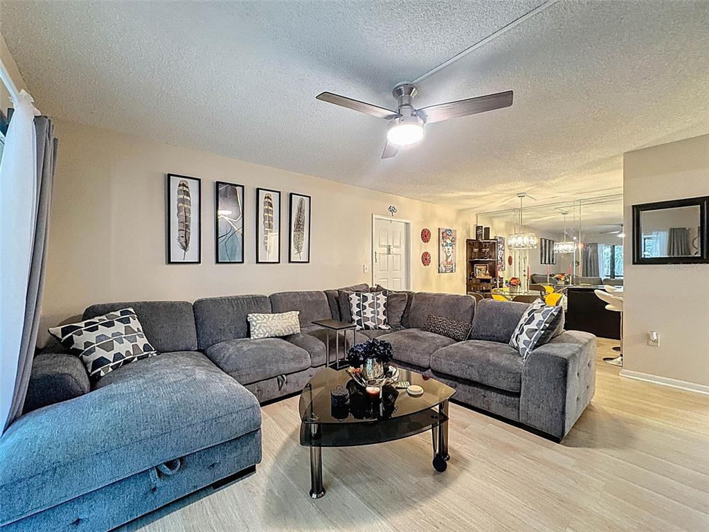 A living room features a large gray sectional sofa, a glass coffee table, and wall art — 3188 LAKE PINE WAY S UNIT B1, TARPON SPRINGS, FL