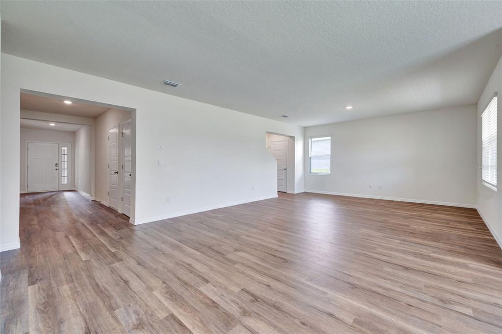 An open-concept living area features light-colored walls, wood-look flooring, and a view of the entryway — 3521 RODEN ROAD, HAINES CITY, FL