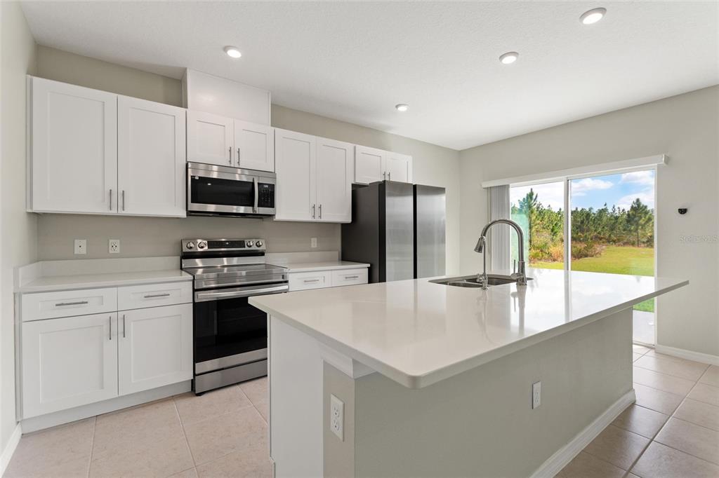 A modern kitchen features white cabinets, stainless steel appliances, a quartz island, and tile flooring — 4201 CALLIANDRA DRIVE, INDIAN LAKE ESTATES, FL