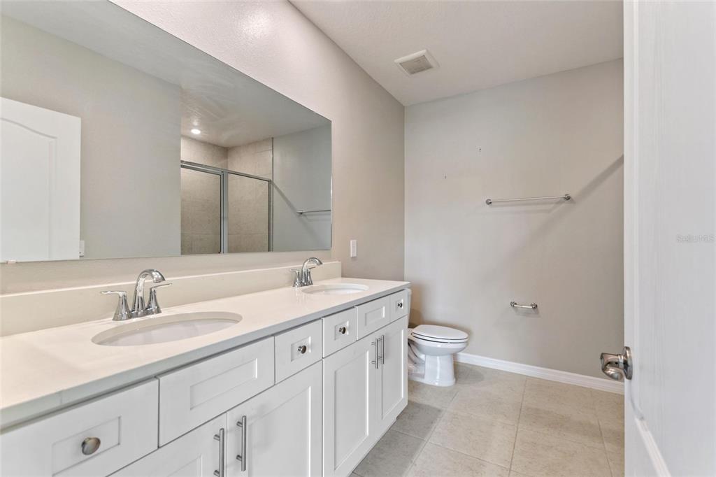 A bathroom features a double vanity with white cabinets, a large mirror, and a toilet — 4201 CALLIANDRA DRIVE, INDIAN LAKE ESTATES, FL