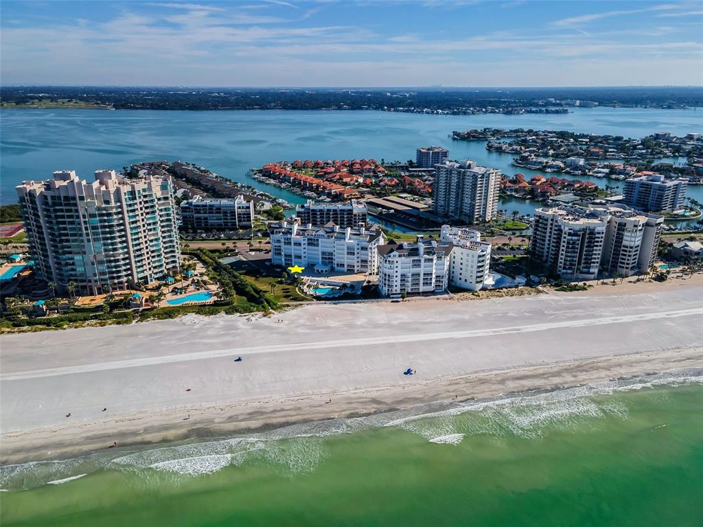 An aerial view shows a coastal resort area with high-rise buildings, a beach, and a road — 1582 GULF BOULEVARD UNIT 1106, CLEARWATER BEACH, FL