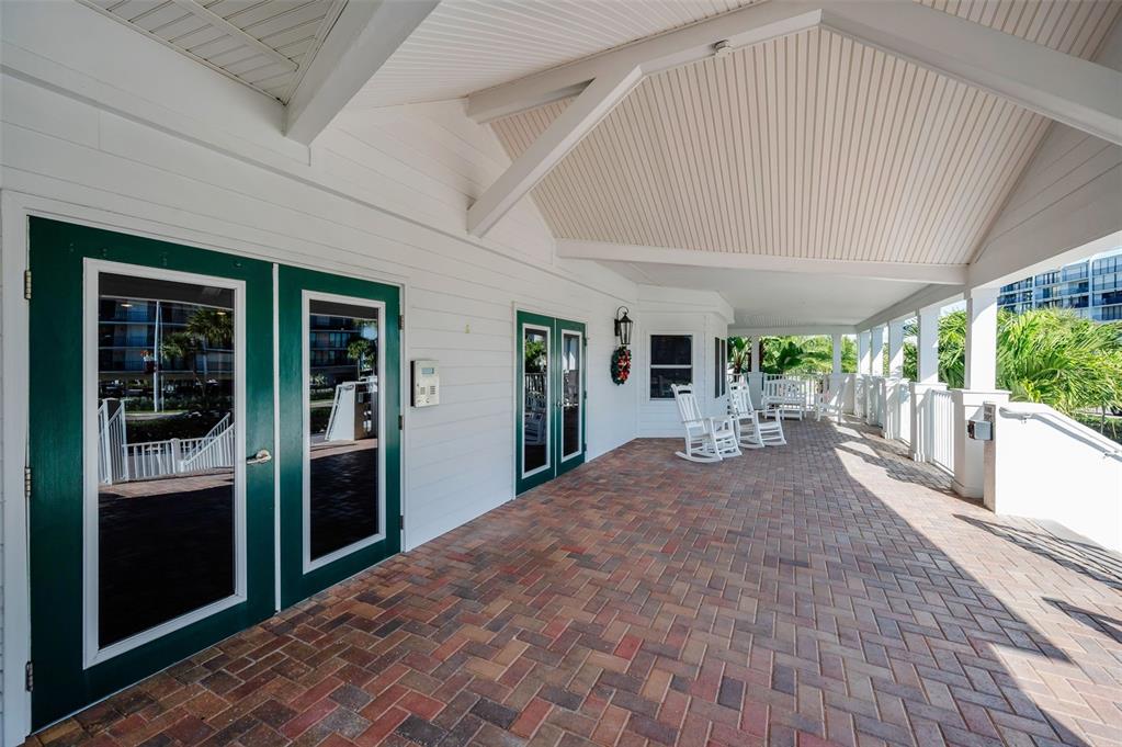 A covered brick patio features white siding, green-trimmed glass doors, and several white rocking chairs — 1582 GULF BOULEVARD UNIT 1106, CLEARWATER BEACH, FL