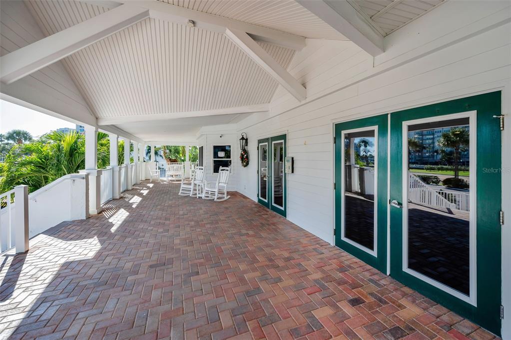 A covered brick patio features white rocking chairs and green-framed glass doors — 1582 GULF BOULEVARD UNIT 1106, CLEARWATER BEACH, FL
