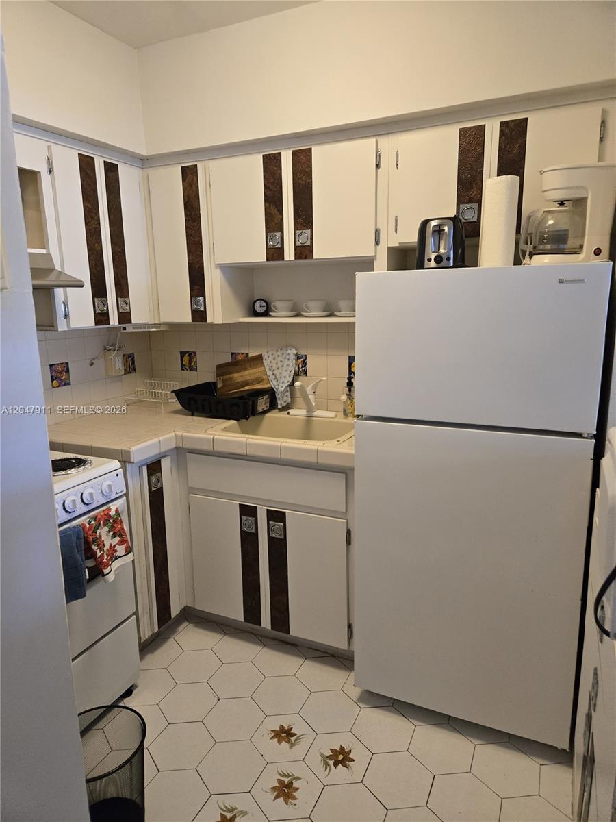 A small kitchen features white cabinets with dark accents, tiled countertops, and white appliances — 2001 S Ocean Dr # 41, Hallandale Beach FL 33009, HALLANDALE BEACH, FL