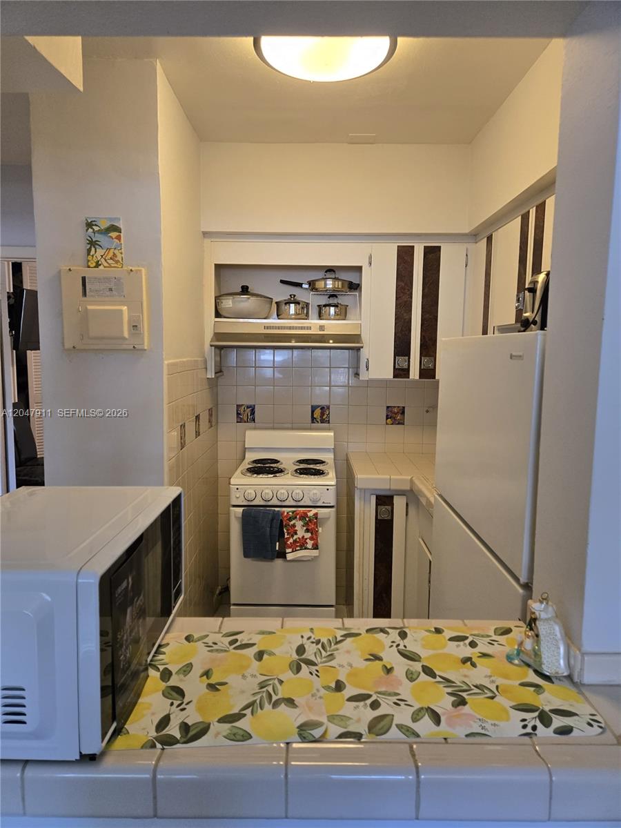 A small kitchen features white appliances, tiled countertops, and a patterned table runner — 2001 S Ocean Dr # 41, Hallandale Beach FL 33009, HALLANDALE BEACH, FL