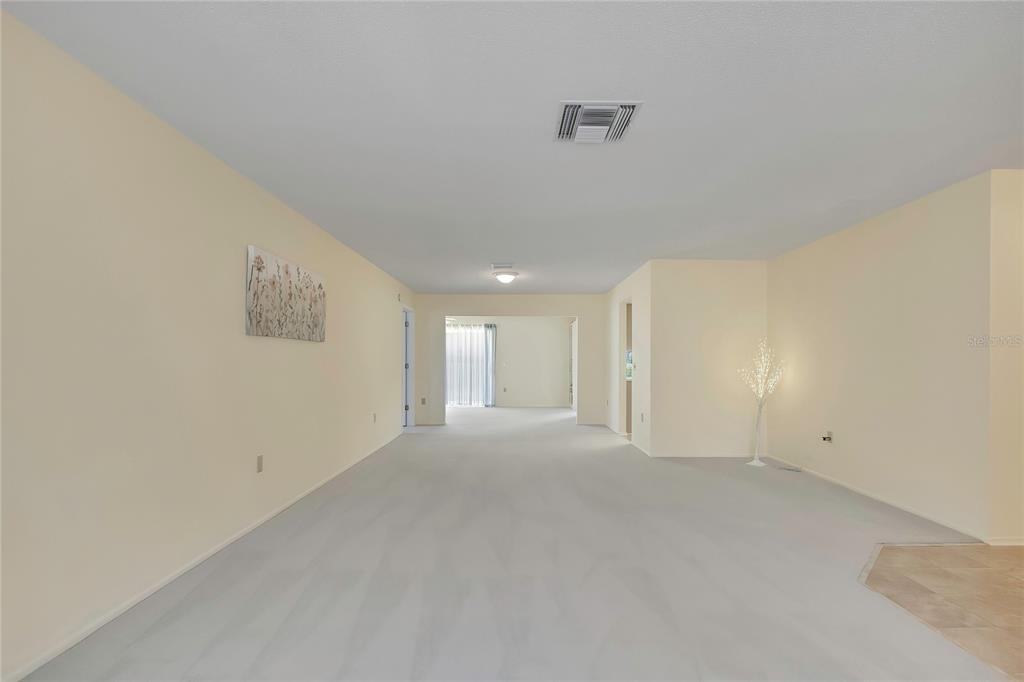 A living room features light-colored carpet, beige walls, a bay window, and a front door — 7103 CROWN OAKS DRIVE, SPRING HILL, FL