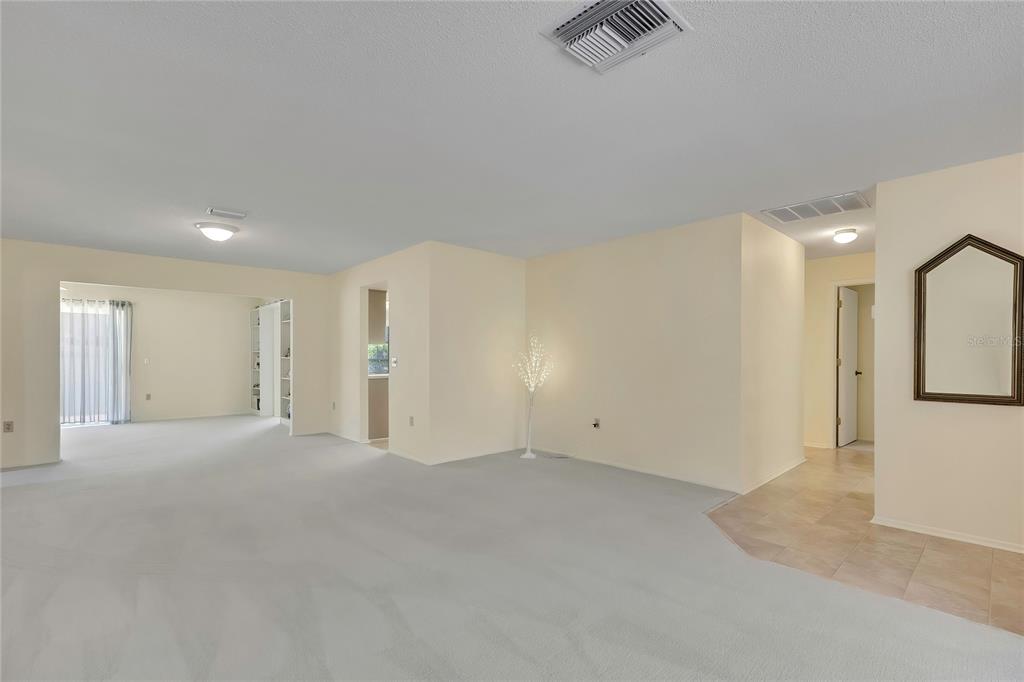 A spacious, carpeted living area with light-colored walls, a ceiling vent, and a sliding glass door — 7103 CROWN OAKS DRIVE, SPRING HILL, FL