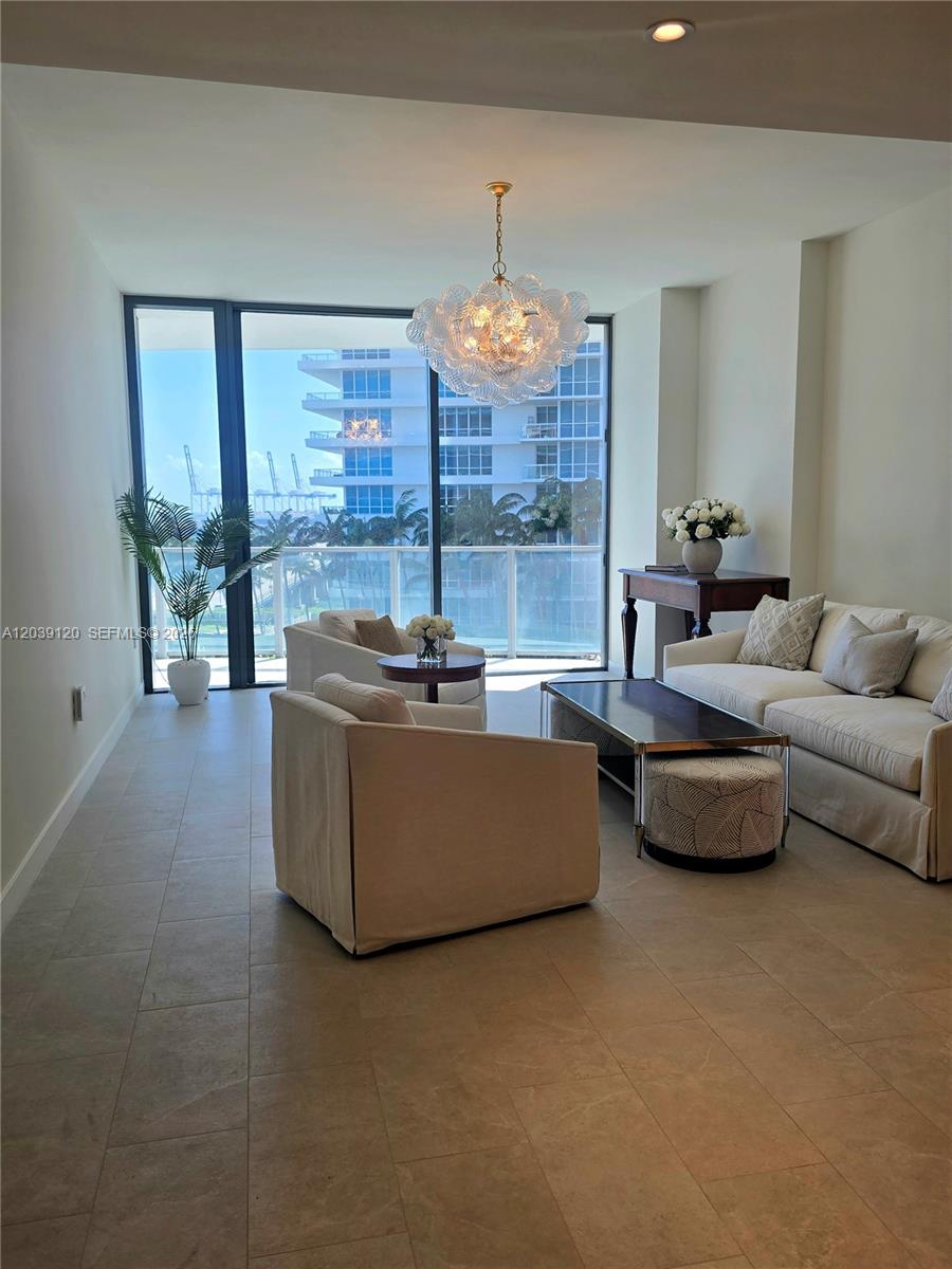 A bright living room features floor-to-ceiling windows, tile flooring, and a modern glass chandelier — 500 Alton Rd # 904, Miami Beach FL 33139, MIAMI BEACH, FL