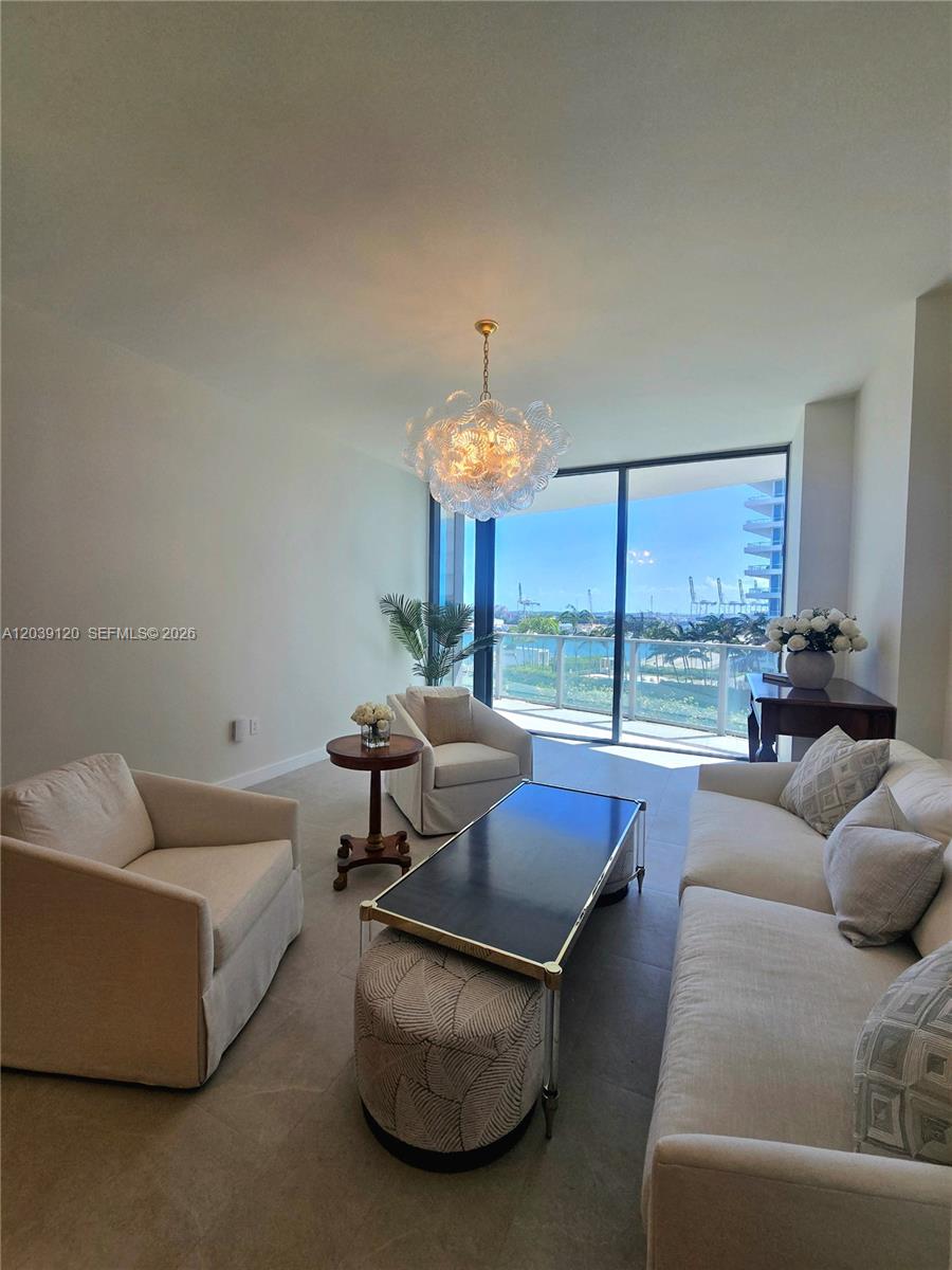 A living room features neutral furniture, a glass-topped coffee table, and a balcony overlooking water — 500 Alton Rd # 904, Miami Beach FL 33139, MIAMI BEACH, FL
