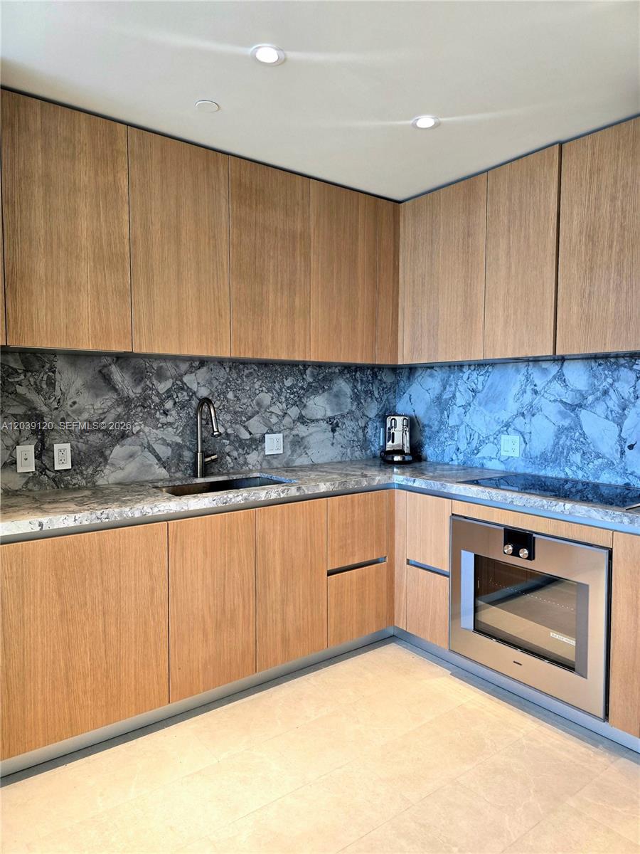 A modern kitchen features light wood cabinets, a gray marble backsplash, and stainless steel appliances — 500 Alton Rd # 904, Miami Beach FL 33139, MIAMI BEACH, FL
