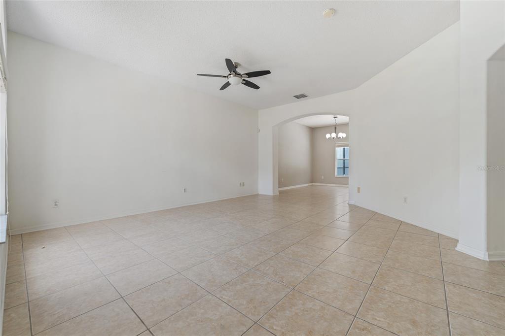An empty living room with white walls, beige tile flooring, and a ceiling fan — 14539 UNBRIDLED DRIVE, ORLANDO, FL