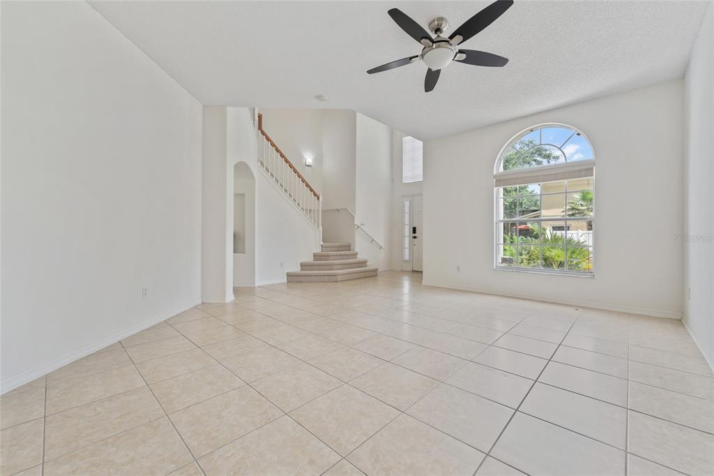 A bright, tiled living room features a high ceiling, a ceiling fan, and a staircase — 14539 UNBRIDLED DRIVE, ORLANDO, FL