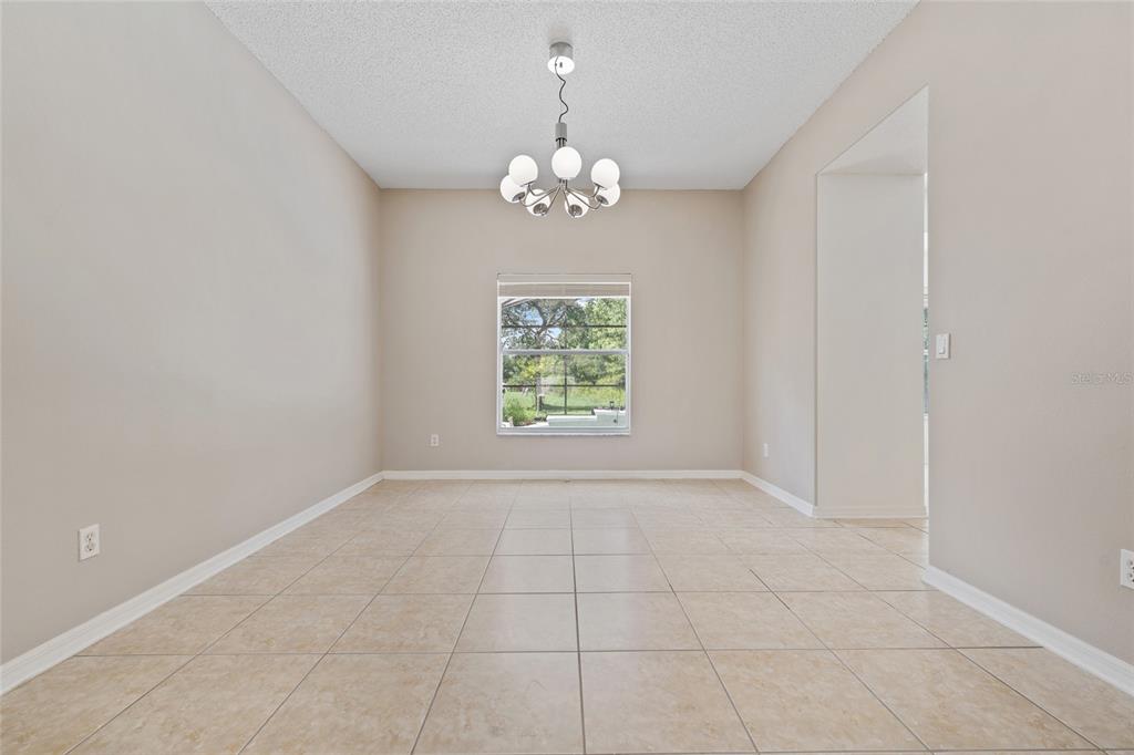 An empty dining room features beige walls, tile flooring, a central chandelier, and a window — 14539 UNBRIDLED DRIVE, ORLANDO, FL