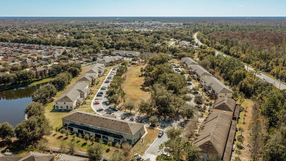 An aerial view shows multiple multi-story residential townhome buildings surrounded by trees and a pond — 2896 TANZANITE TERRACE, KISSIMMEE, FL