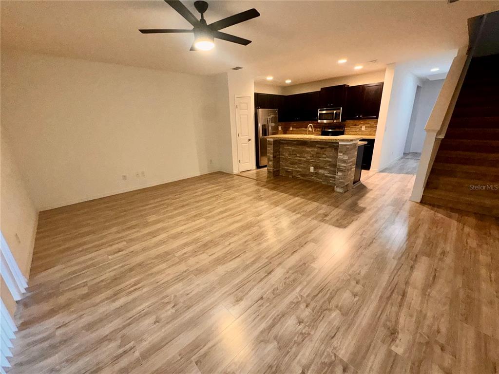An open-concept living area features wood-look flooring, a kitchen island, and a staircase — 2896 TANZANITE TERRACE, KISSIMMEE, FL
