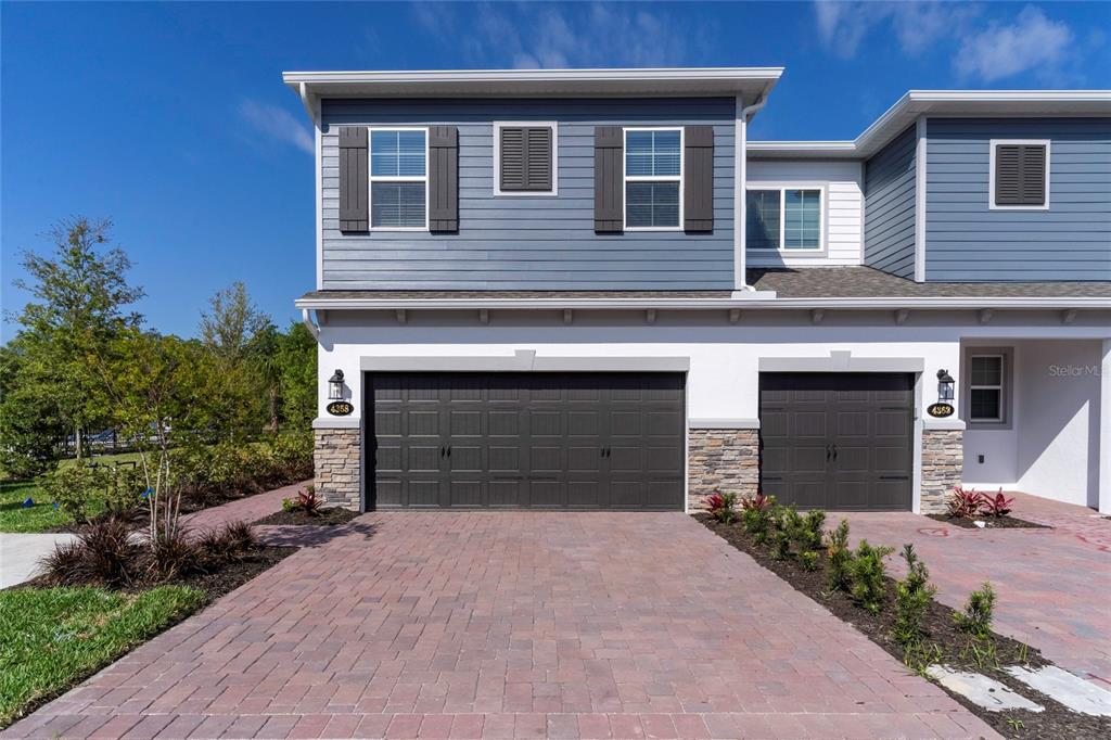 A two-story townhouse exterior features blue siding, stone accents, and two dark garage doors — 4358 CAMPSITE LOOP, ORLANDO, FL