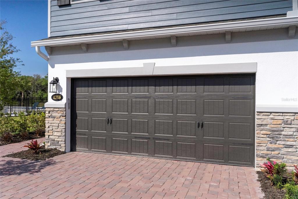 A dark brown garage door is set into a house with stone and white siding — 4358 CAMPSITE LOOP, ORLANDO, FL