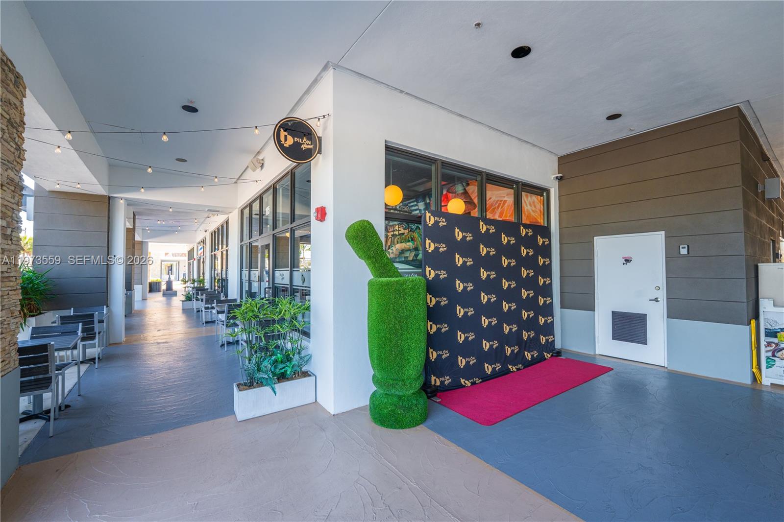 An outdoor patio area features a green topiary mortar and pestle next to a branded backdrop — 12850 sw 128th st, Miami FL 33186, MIAMI, FL