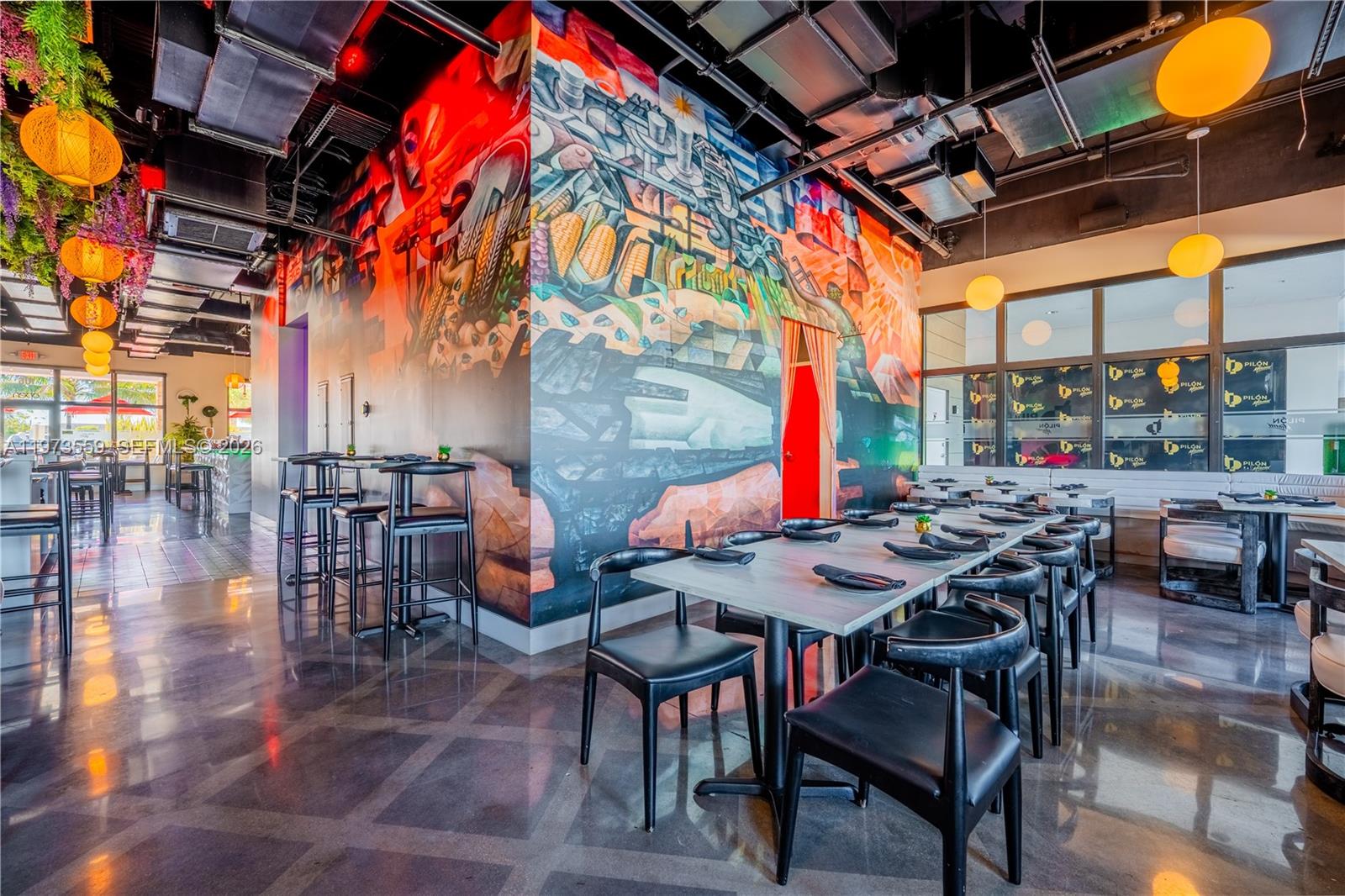 A restaurant interior features a large colorful mural, black chairs, and modern pendant lighting — 12850 sw 128th st, Miami FL 33186, MIAMI, FL