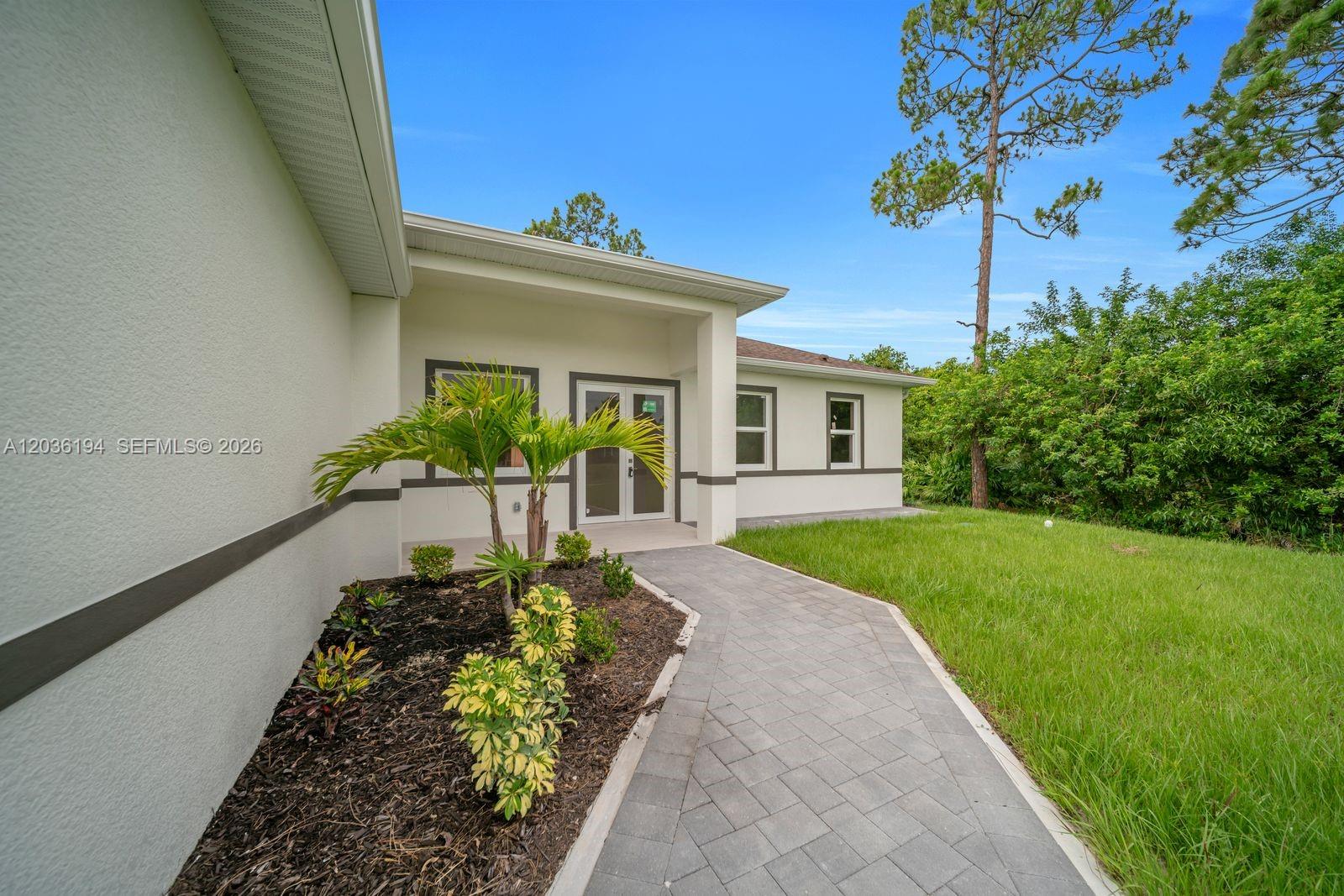 A paved walkway leads to the front entrance of a light-colored house with landscaping — 2715 10th ST W, Lehigh Acres FL 33971, LEHIGH ACRES, FL