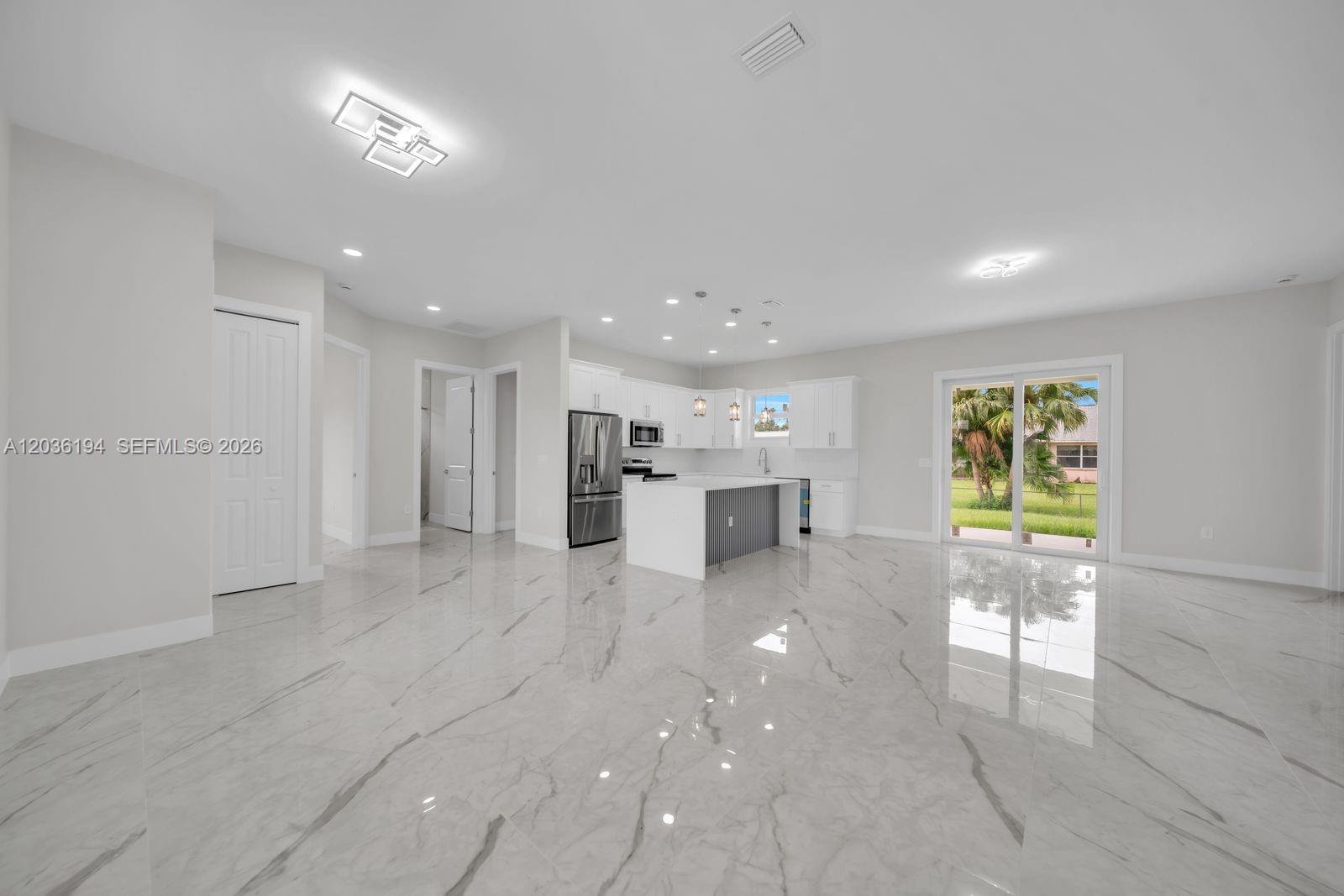 A modern open-concept kitchen features white cabinetry, a central island, and polished marble-style flooring — 2715 10th ST W, Lehigh Acres FL 33971, LEHIGH ACRES, FL