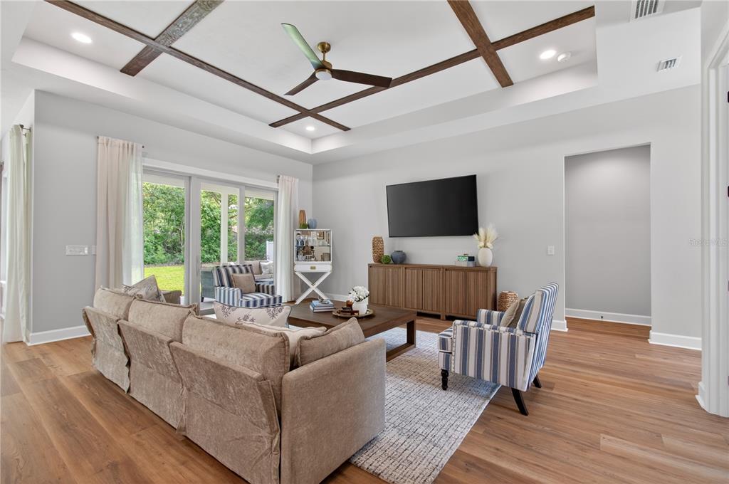 A living room features a coffered ceiling, wood-look flooring, and a large wall-mounted television — 14098 SW 7TH PLACE, NEWBERRY, FL