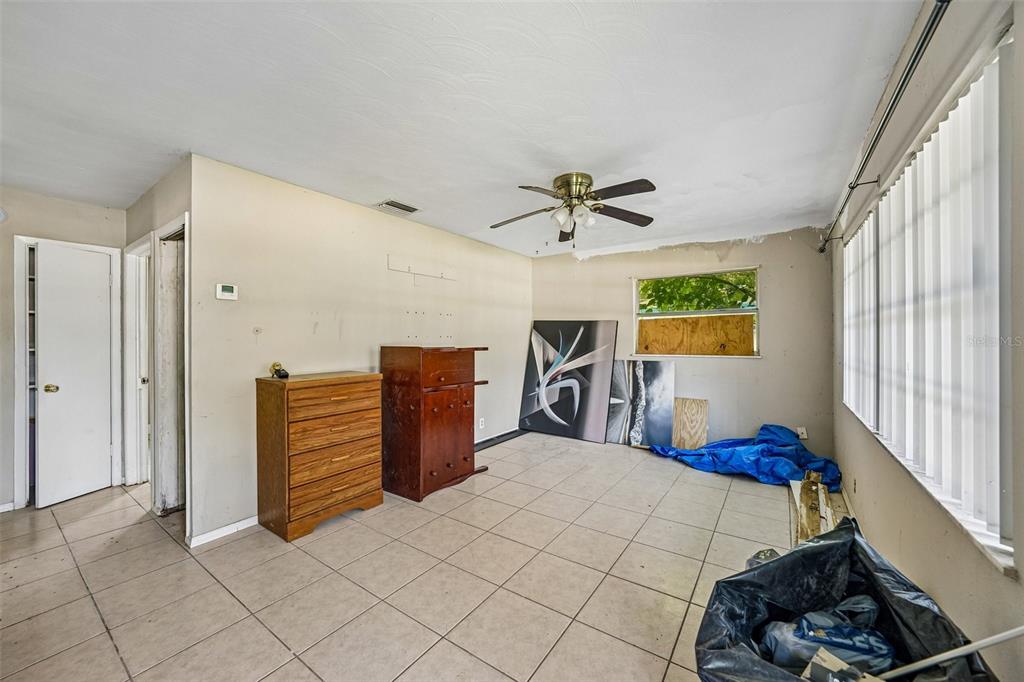 A sparsely furnished room features tile flooring, a ceiling fan, and a boarded-up window — 18748 ROSEPHIL ST, SPRING HILL, FL