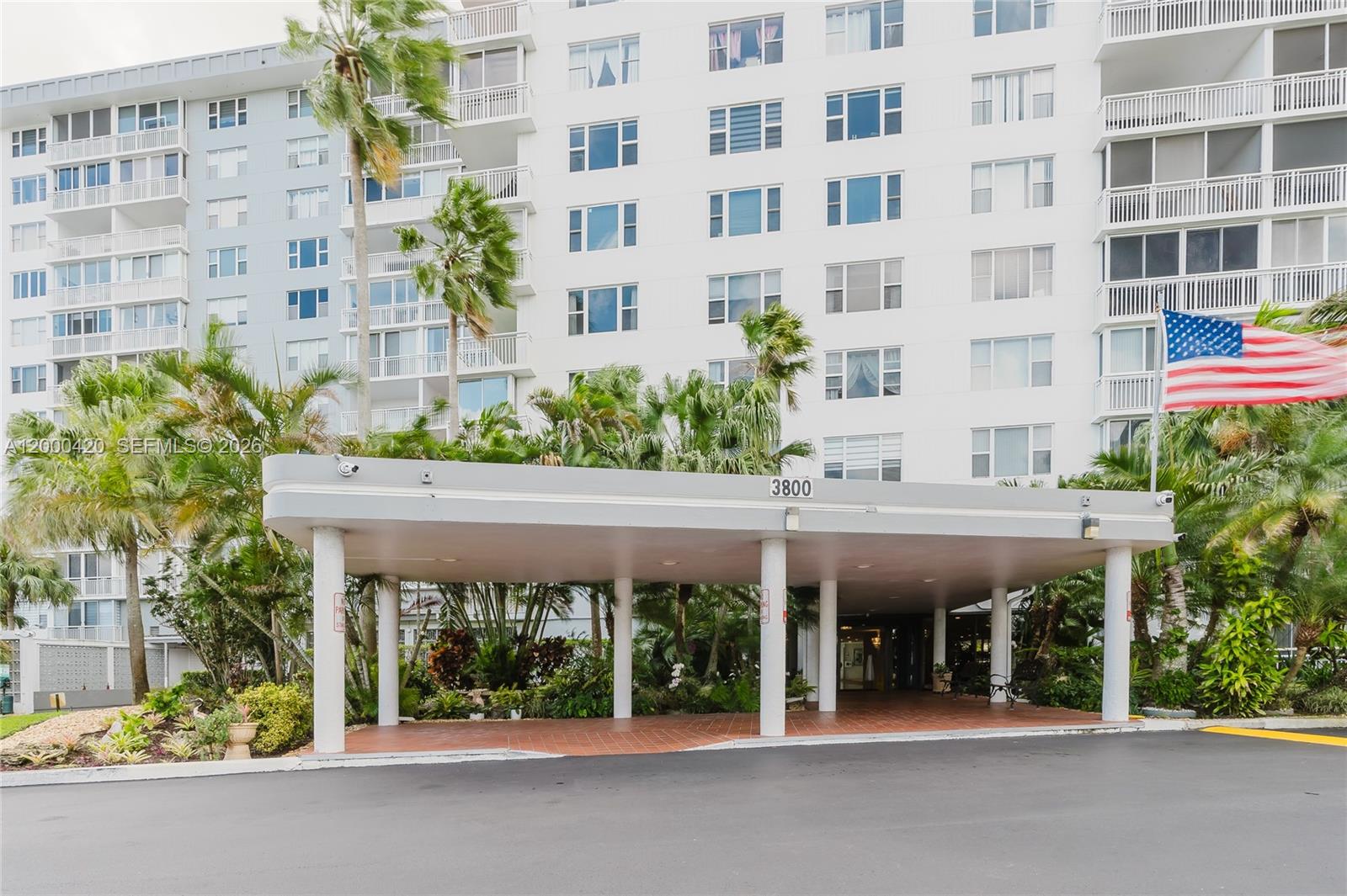 A multi-story white apartment building features a covered entrance with columns and a large flag — 3800 Hillcrest Dr # 411, Hollywood FL 33021, HOLLYWOOD, FL