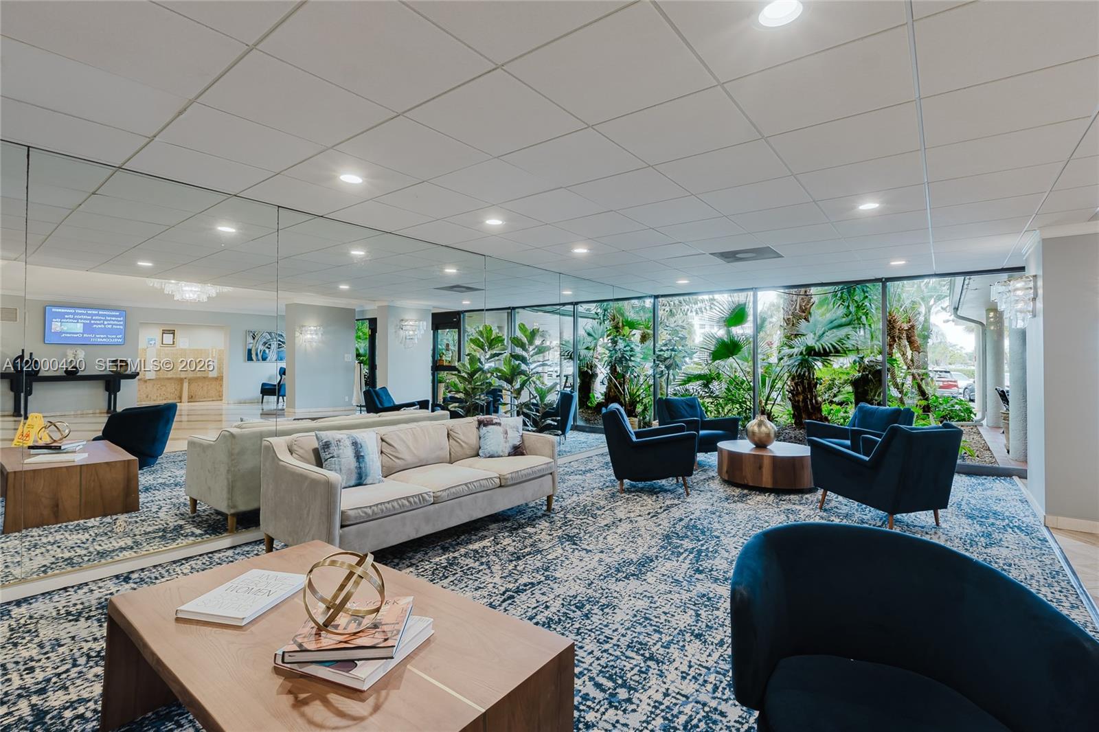 A lobby features a beige sofa, blue armchairs, a patterned rug, and a mirrored wall — 3800 Hillcrest Dr # 411, Hollywood FL 33021, HOLLYWOOD, FL