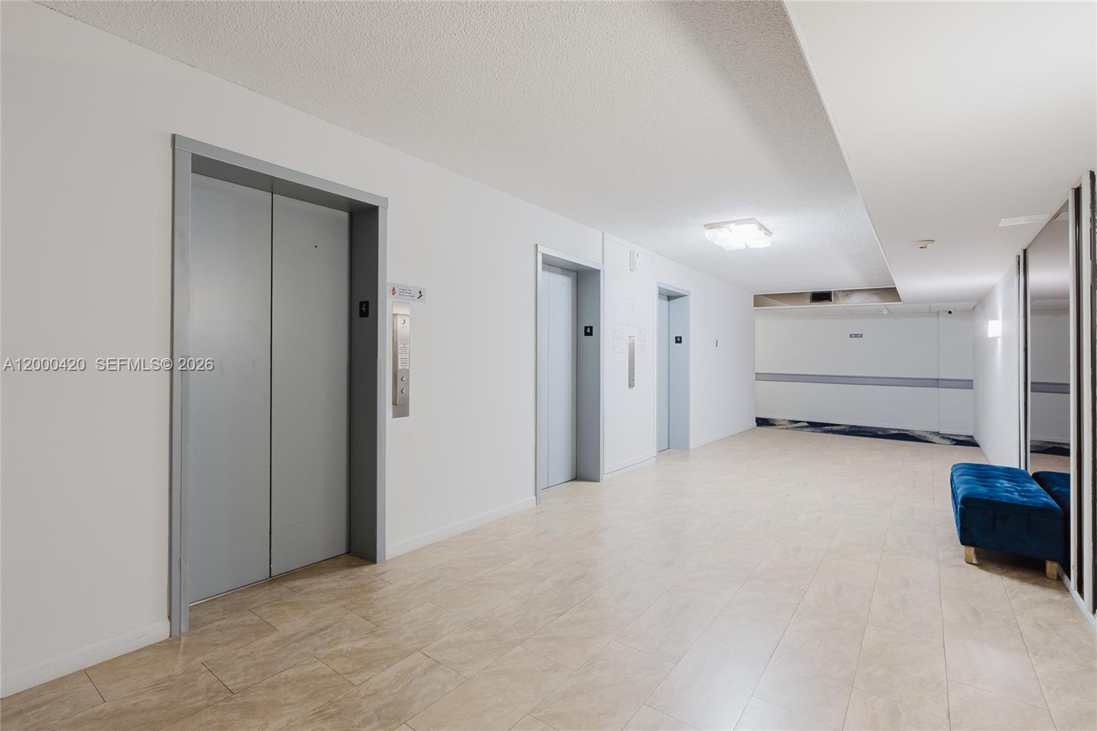 A hallway features light tile flooring, three gray elevator doors, and a blue velvet bench — 3800 Hillcrest Dr # 411, Hollywood FL 33021, HOLLYWOOD, FL