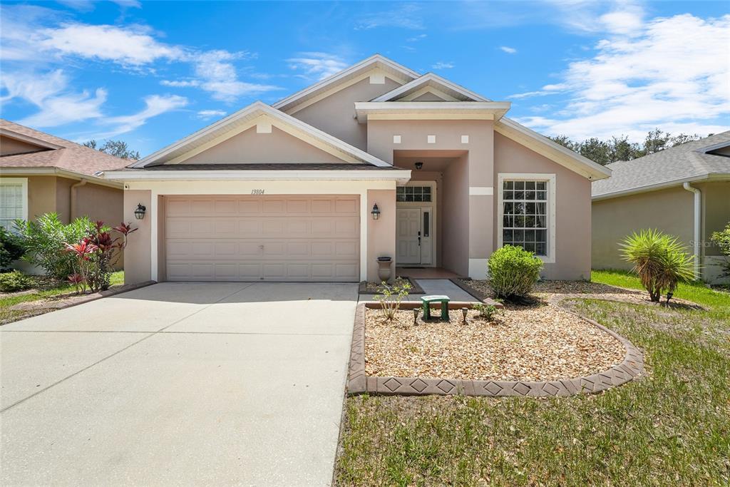A single-story house with a beige stucco exterior, a two-car garage, and a gravel front yard — 13804 SIGLER STREET, RIVERVIEW, FL