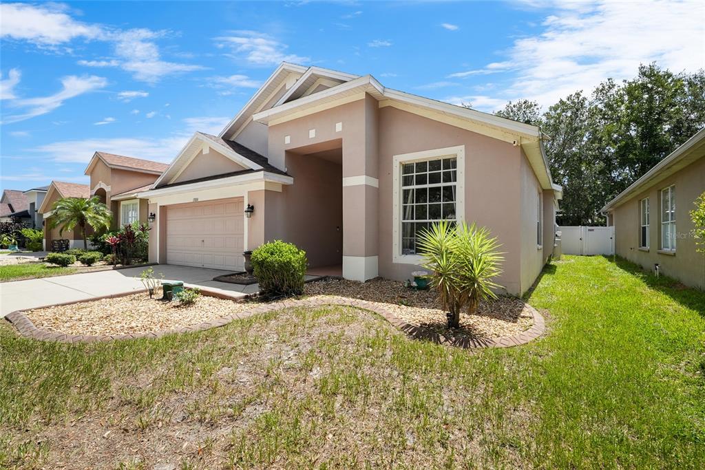 A beige single-story house features a two-car garage, a covered entryway, and a landscaped yard — 13804 SIGLER STREET, RIVERVIEW, FL