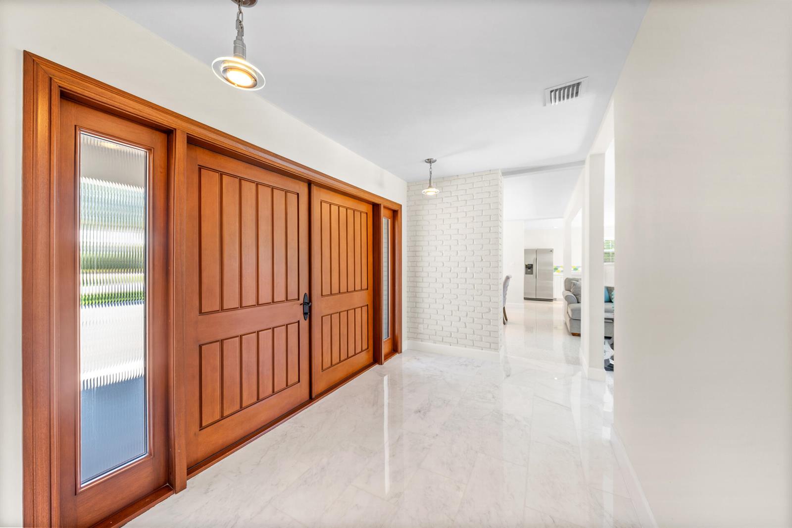 A bright entryway features double wood doors, white marble flooring, and a white brick accent wall — 2259 Ibis Isle Road E, Palm Beach FL 33480, PALM BEACH, FL