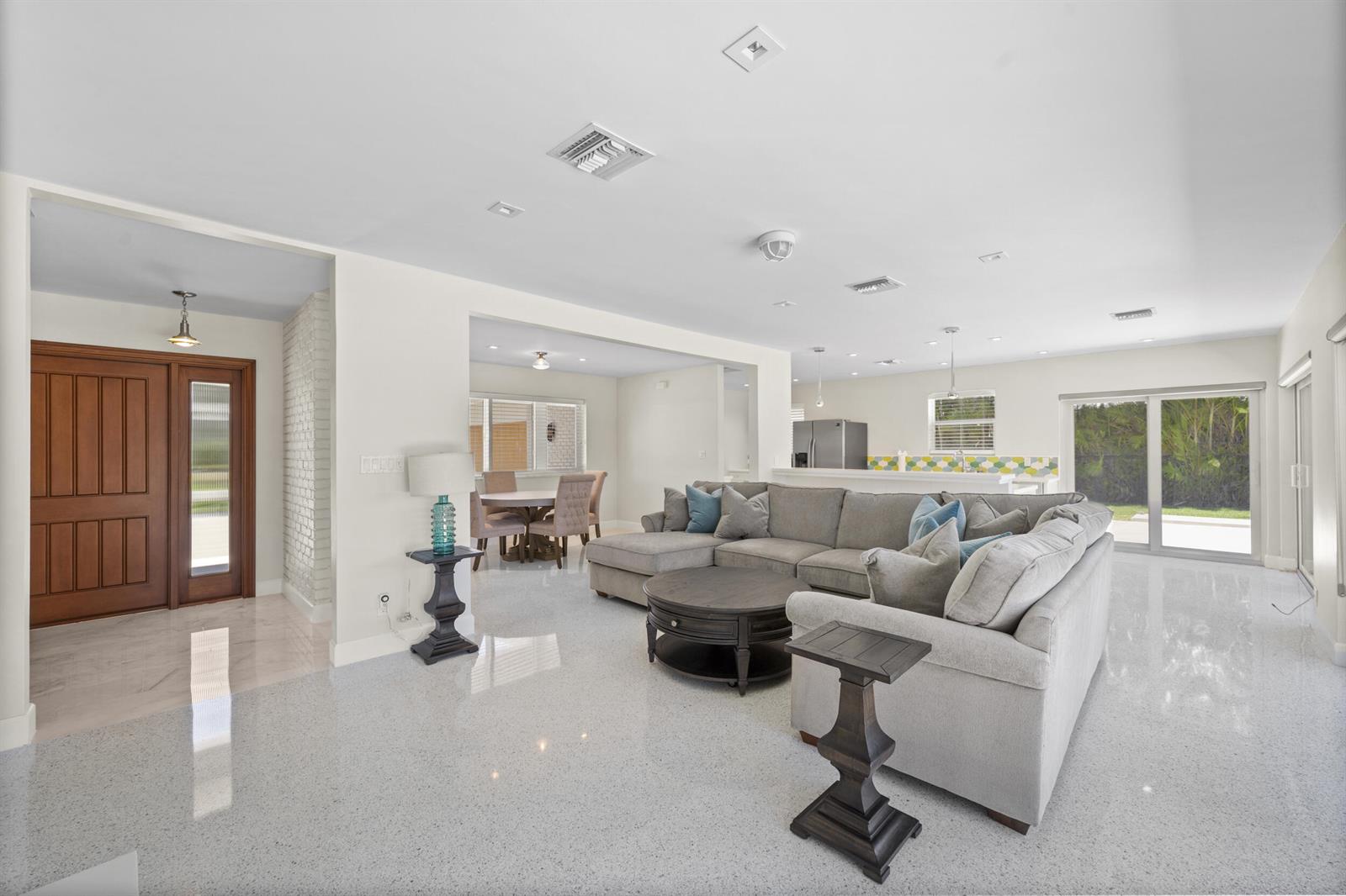 An open-concept living area features a gray sectional sofa, a round coffee table, and terrazzo flooring — 2259 Ibis Isle Road E, Palm Beach FL 33480, PALM BEACH, FL
