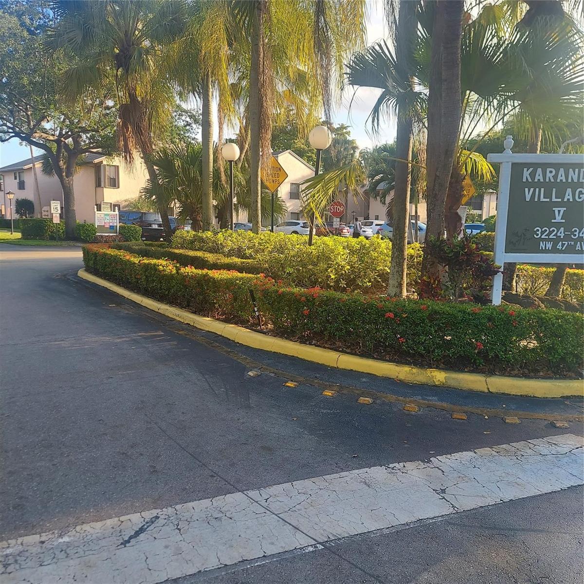 An exterior view of a residential complex entrance with palm trees, landscaping, and signage — 3420 NW 47th Avenue # 3143, Pompano Beach FL 33063, POMPANO BEACH, FL
