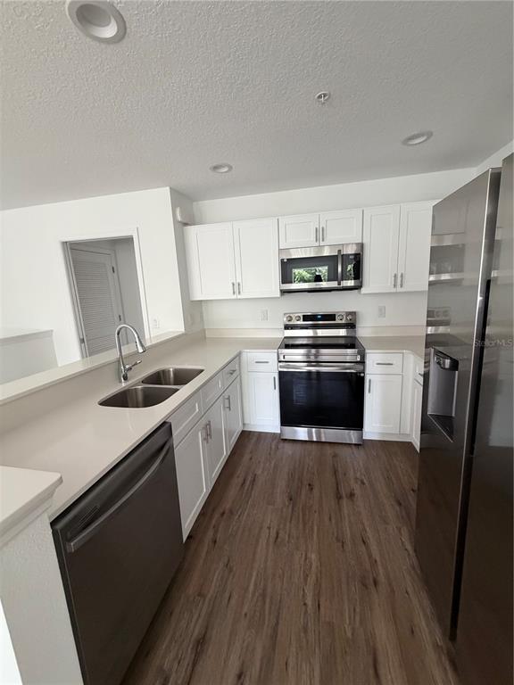 A kitchen features white cabinets, stainless steel appliances, and light countertops over wood-look flooring — 2575 6TH AVENUE DRIVE E, BRADENTON, FL