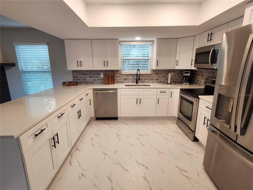 A modern kitchen features white cabinets, stainless steel appliances, and gray subway tile backsplashes — 3071 HURON AVENUE, OLDSMAR, FL