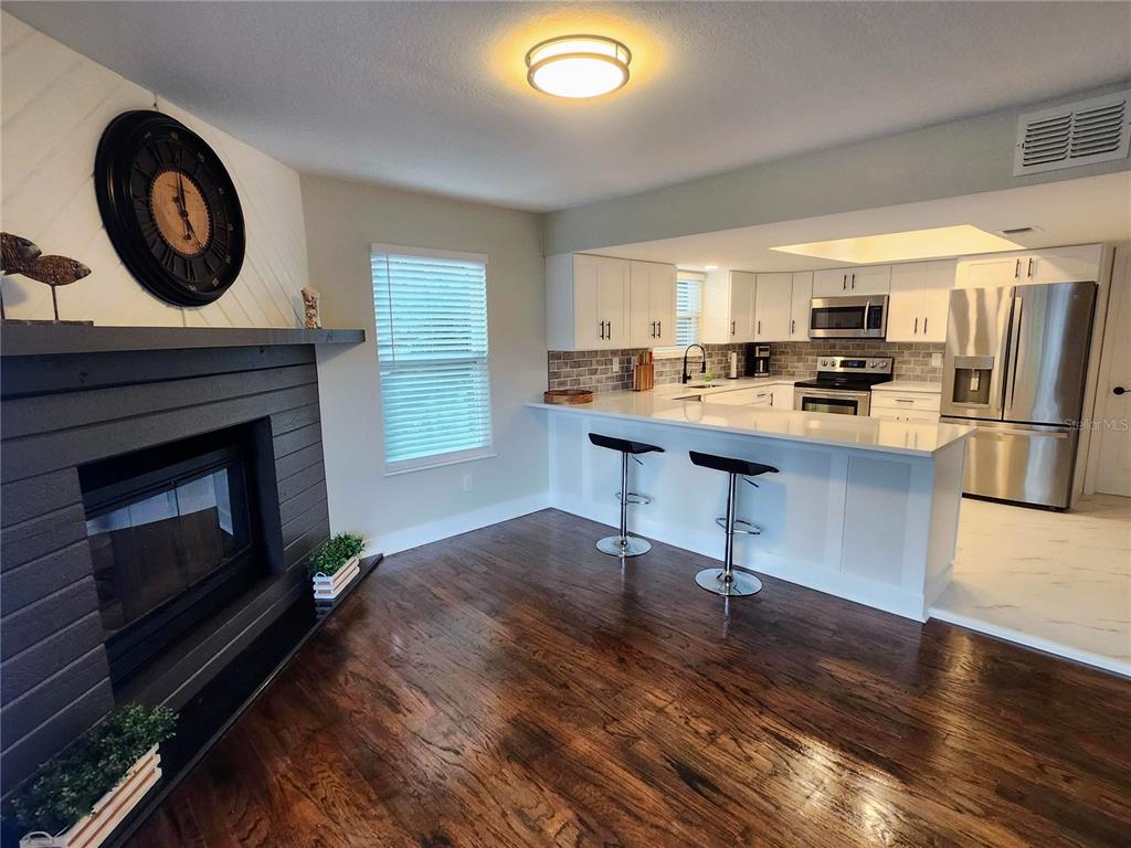 A living room with a fireplace and wood floors opens to a kitchen with white cabinets — 3071 HURON AVENUE, OLDSMAR, FL