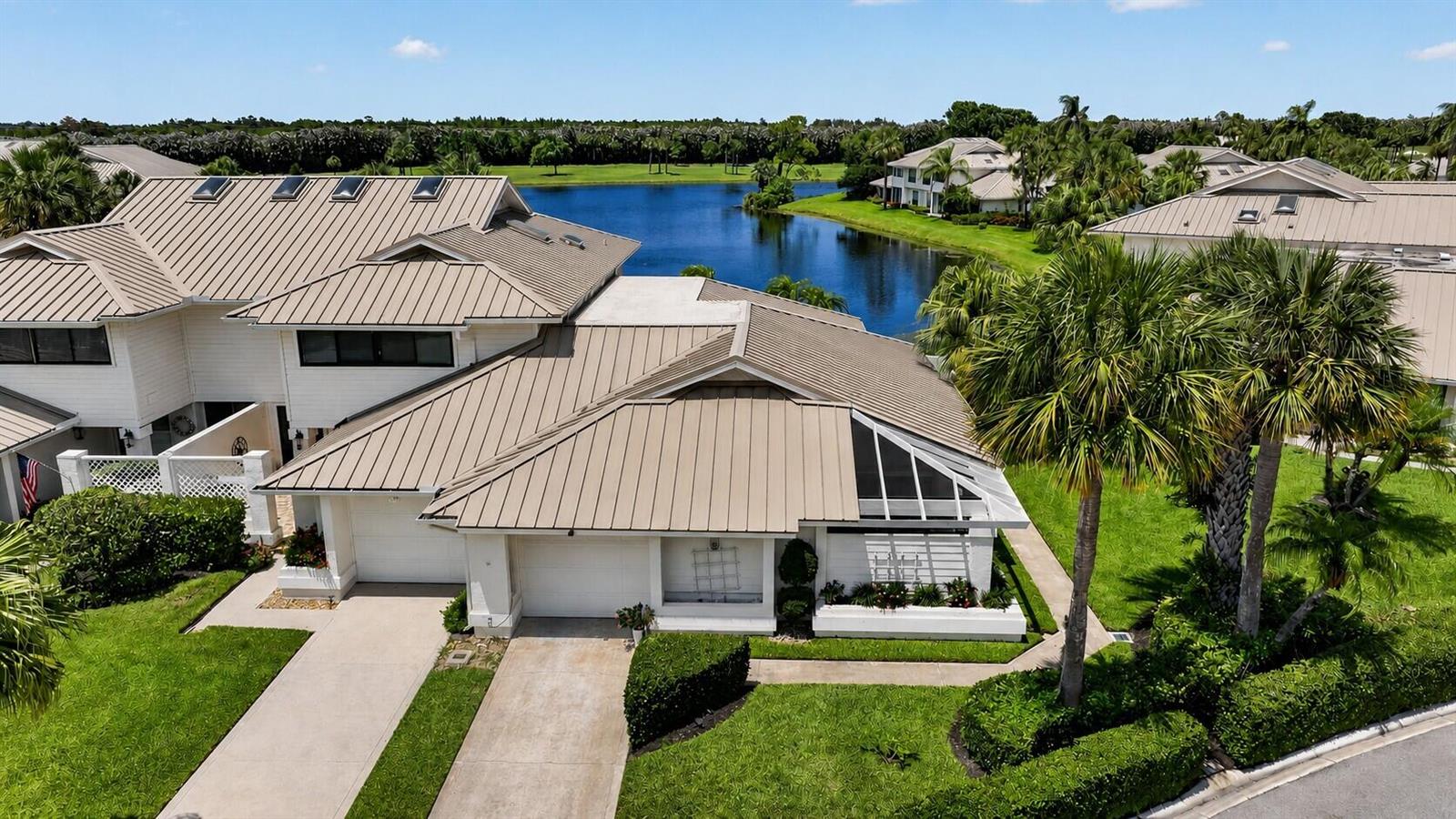 A view of a grassy lawn, palm trees, and a lake behind residential buildings — 5632 SE Foxcross Place, Stuart FL 34997, STUART, FL
