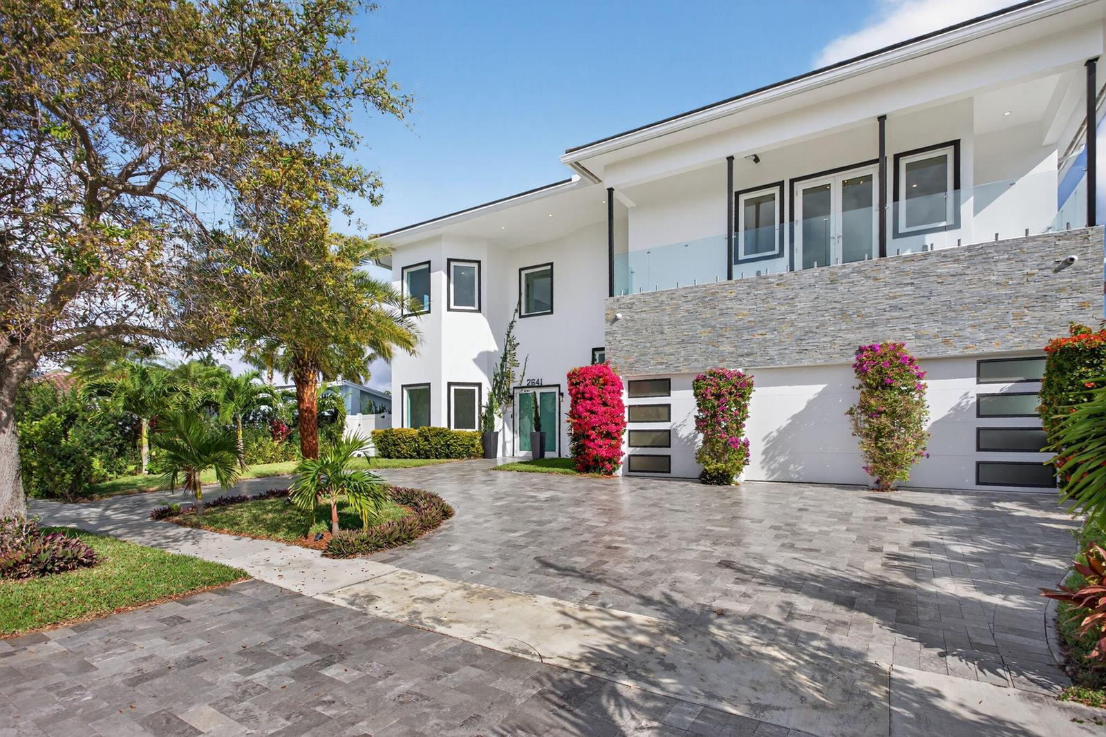 A two-story white house with a stone facade, glass balcony, and a paved driveway — 2641 NE 48th Street, Lighthouse Point FL 33064, LIGHTHOUSE POINT, FL