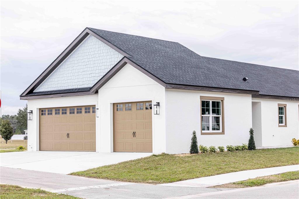 A white house exterior features two tan garage doors, a shingled roof, and green landscaping — 10611 GRAND OAKS BOULEVARD, OXFORD, FL