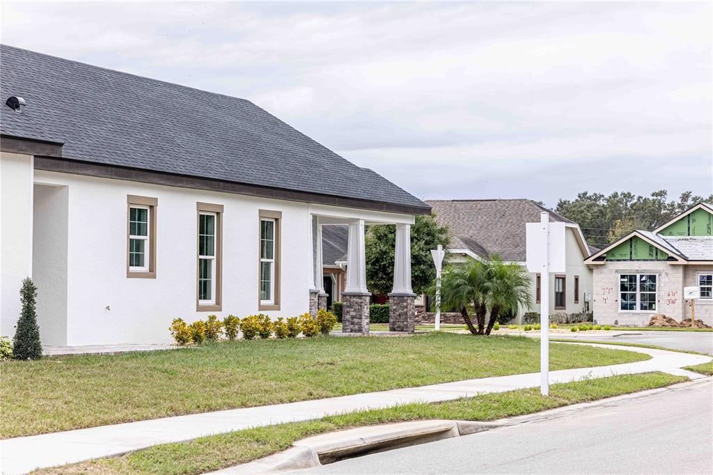 A white stucco house with a dark shingled roof and stone-based columns stands near a construction site — 10611 GRAND OAKS BOULEVARD, OXFORD, FL