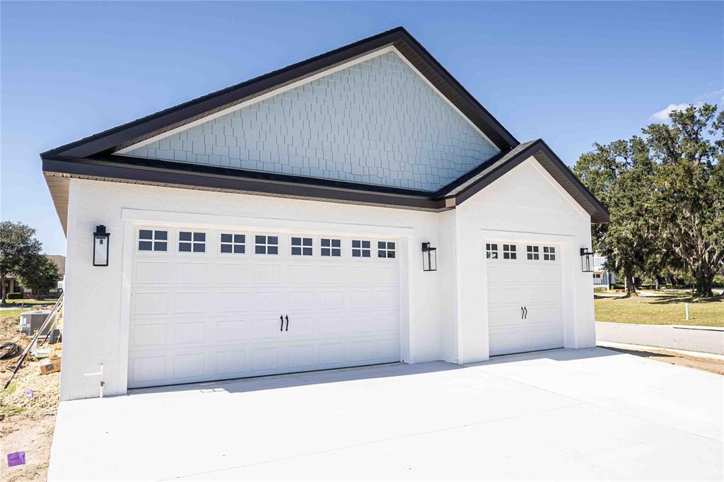 A white house exterior features a three-car garage with light blue shingle siding above — 10611 GRAND OAKS BOULEVARD, OXFORD, FL