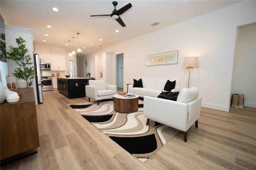 An open-concept living room and kitchen feature white cabinetry, a dark island, and wood flooring — 10611 GRAND OAKS BOULEVARD, OXFORD, FL