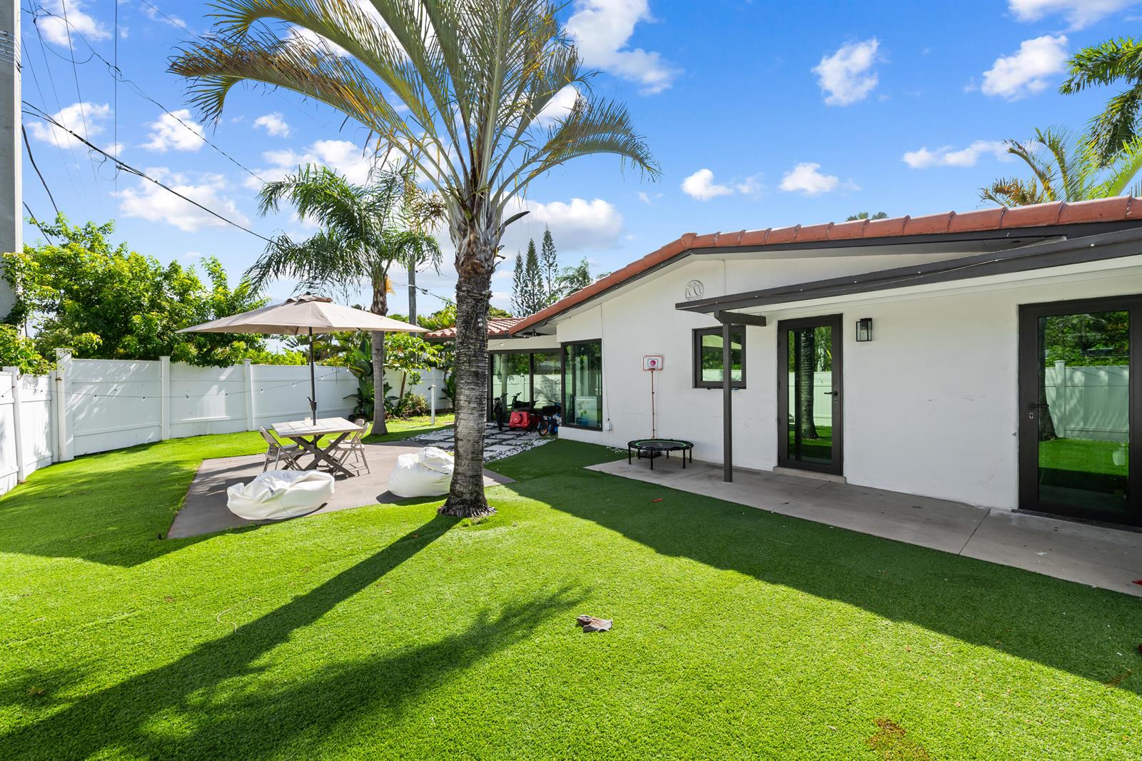 A backyard with artificial turf, a palm tree, a patio table, and a white house — 2601 NE 8th Court, Pompano Beach FL 33062, POMPANO BEACH, FL