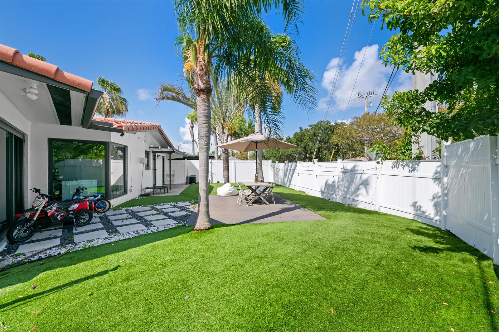 A backyard features artificial turf, a paved patio with an umbrella, and a palm tree — 2601 NE 8th Court, Pompano Beach FL 33062, POMPANO BEACH, FL
