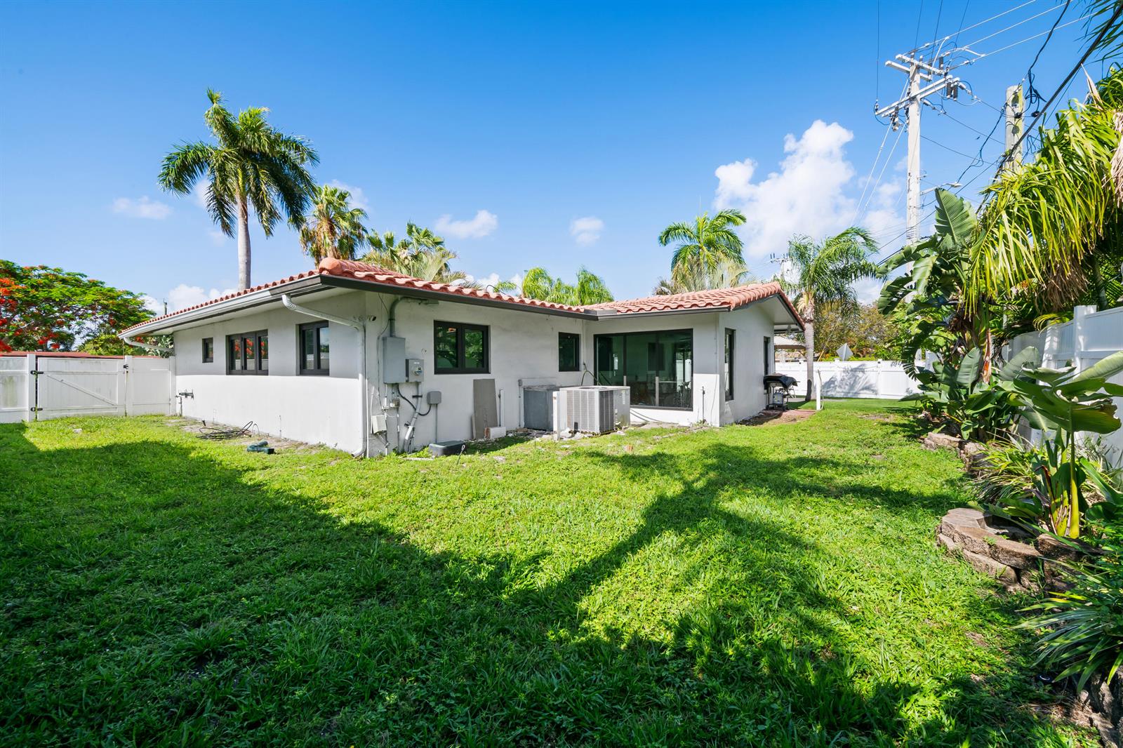 The exterior of a white, single-story house with a tiled roof and a grassy backyard — 2601 NE 8th Court, Pompano Beach FL 33062, POMPANO BEACH, FL
